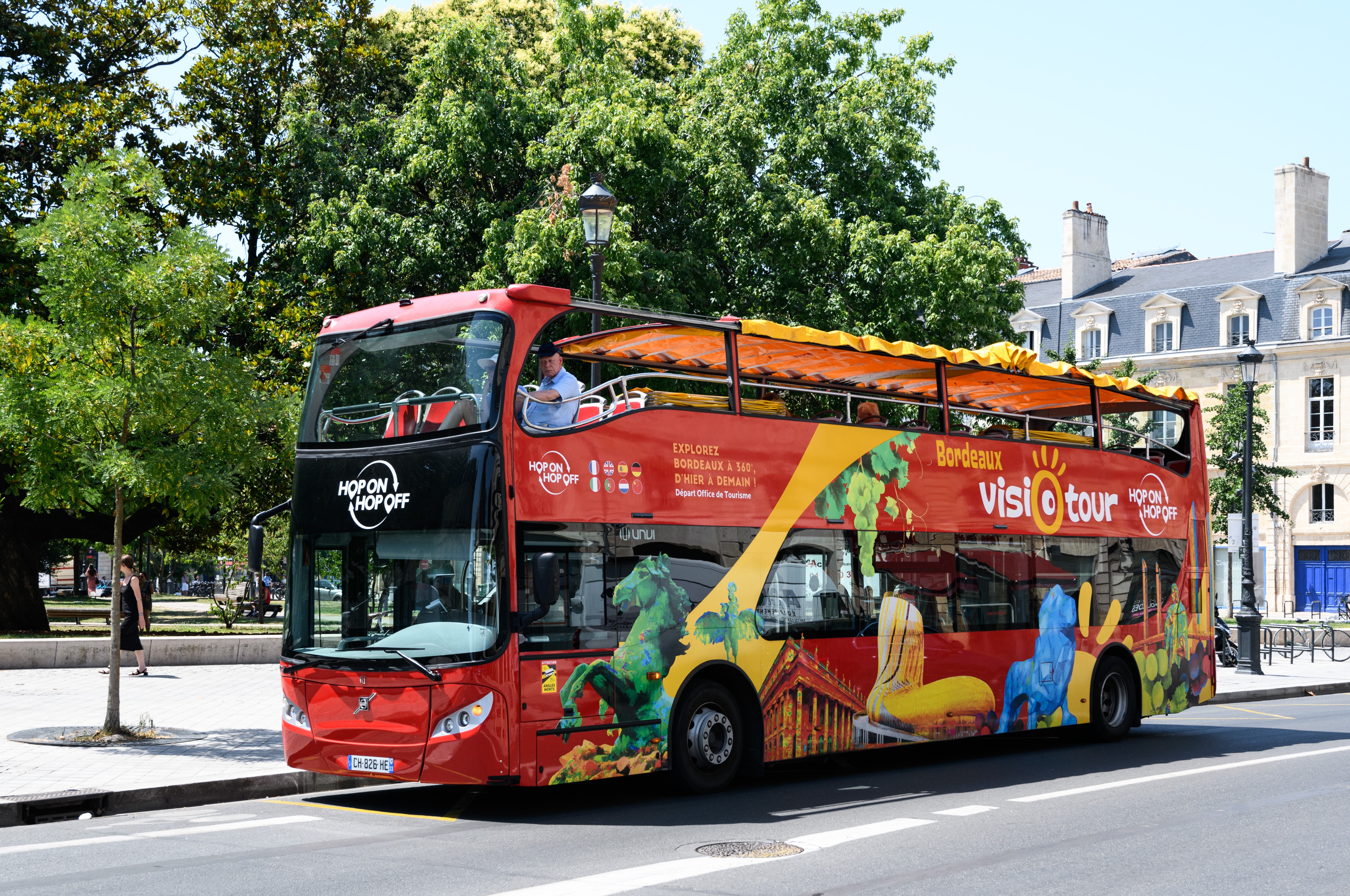 Bus rouges Bordeaux Visiotour stationnés sous les arbres.